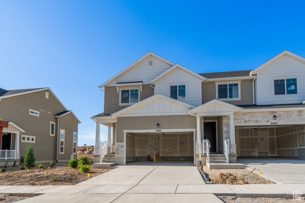 View of front of property with board and batten siding, driveway, a garage, and stone siding