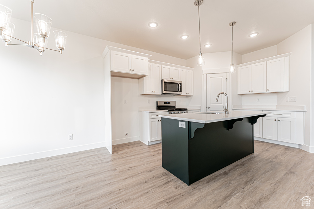 Kitchen with stainless steel appliances, light wood-type flooring, white cabinets, a kitchen breakfast bar, and recessed lighting