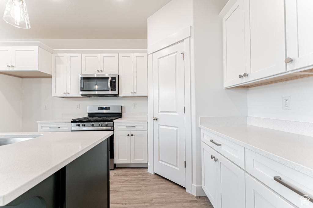 Kitchen with stainless steel appliances, light countertops, white cabinetry, and light wood finished floors
