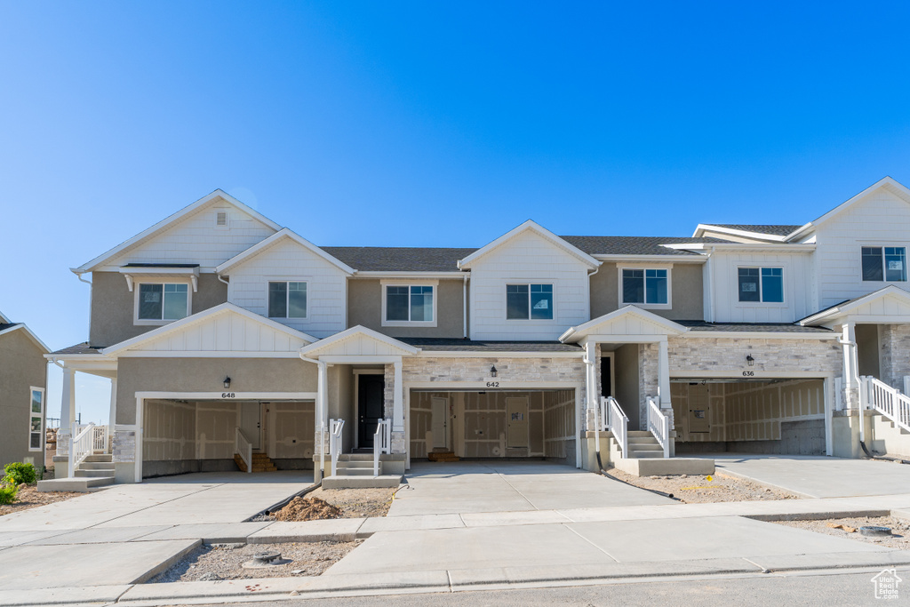 Townhome / multi-family property with a garage, board and batten siding, driveway, and stone siding