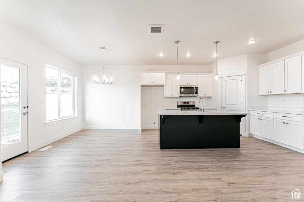 Kitchen with appliances with stainless steel finishes, a chandelier, light wood-type flooring, light countertops, and recessed lighting