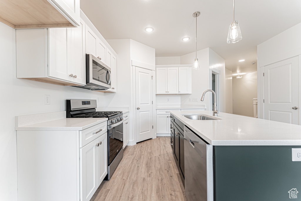 Kitchen featuring stainless steel appliances, light wood-style flooring, light countertops, a center island with sink, and recessed lighting