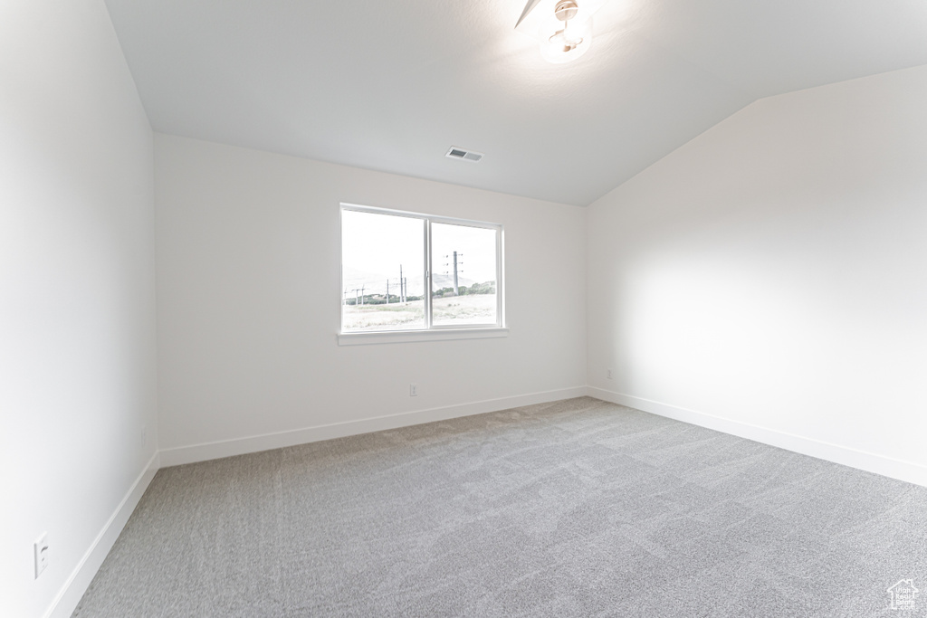 Spare room featuring vaulted ceiling and light colored carpet