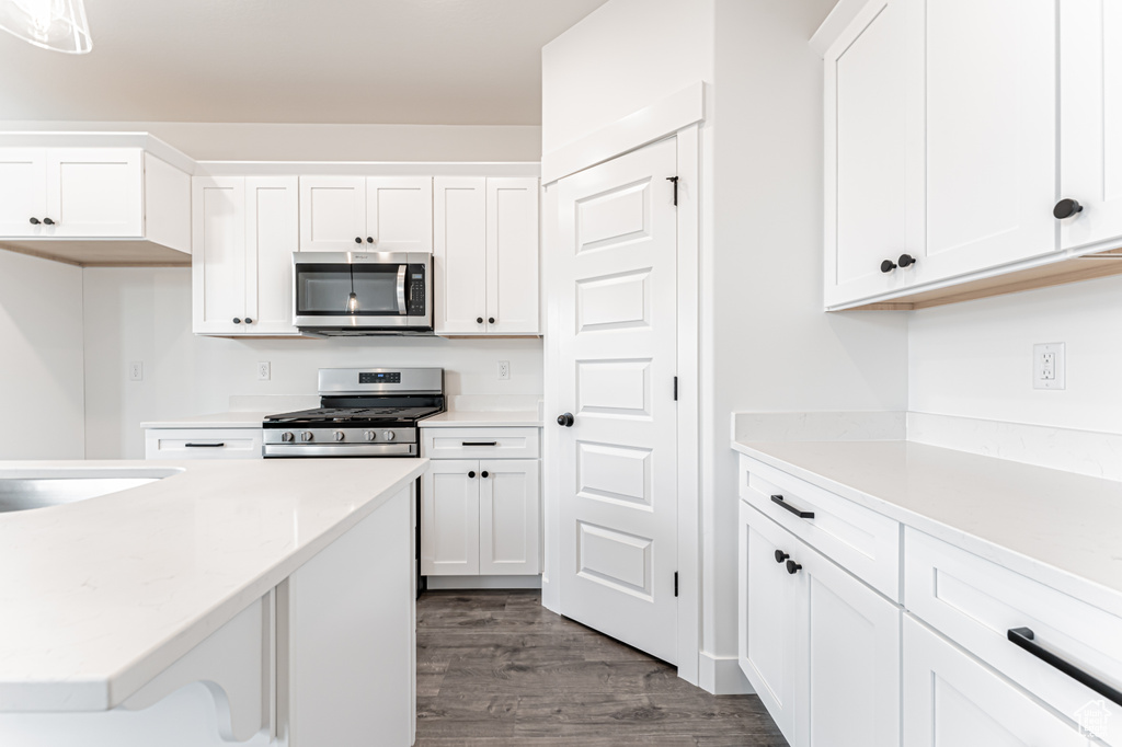 Kitchen featuring appliances with stainless steel finishes, dark wood-style floors, white cabinets, and light countertops