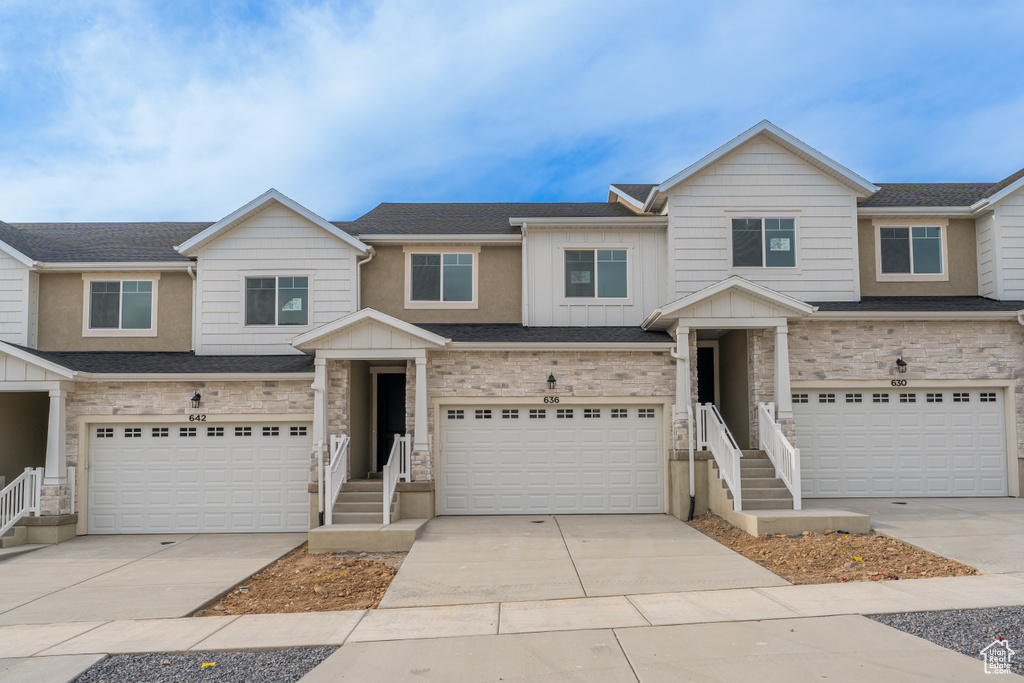 View of property with board and batten siding, an attached garage, stone siding, and driveway