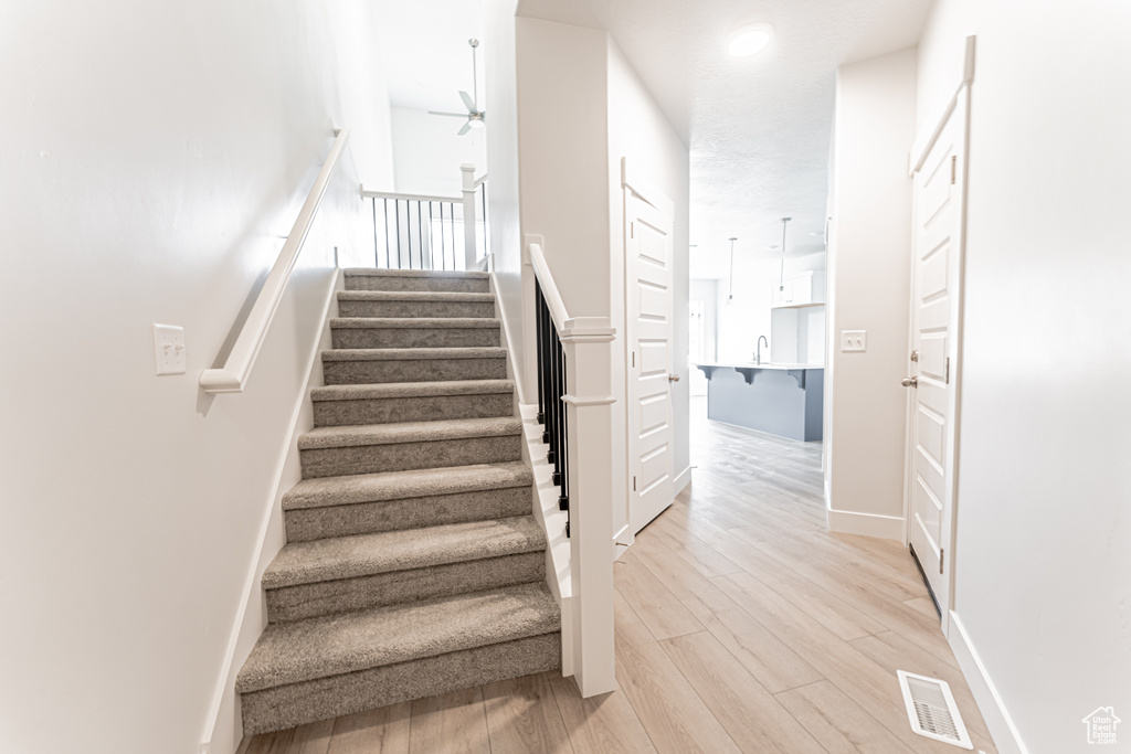 Stairway with a ceiling fan and wood finished floors
