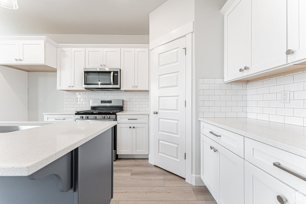 Kitchen with appliances with stainless steel finishes, white cabinets, light wood-style floors, light stone counters, and tasteful backsplash