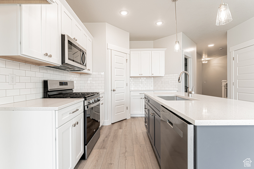 Kitchen with stainless steel appliances, light wood-style flooring, an island with sink, recessed lighting, and decorative light fixtures