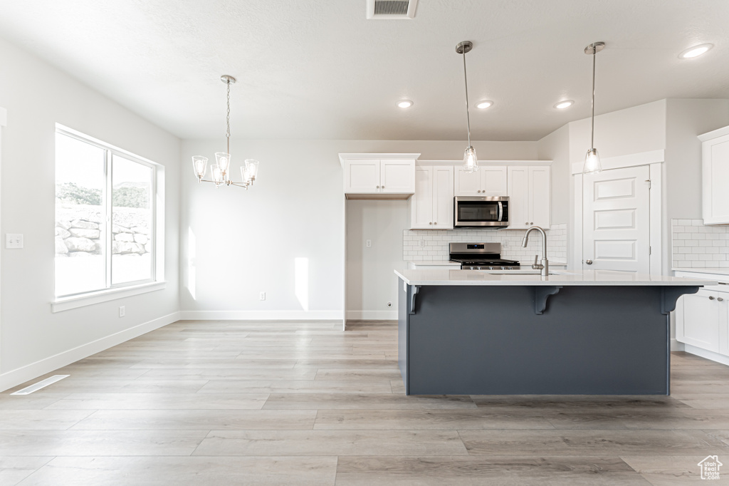 Kitchen featuring appliances with stainless steel finishes, light countertops, white cabinets, a breakfast bar area, and recessed lighting