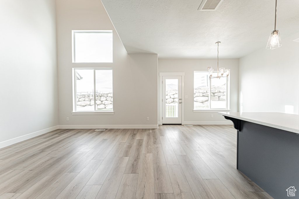 Unfurnished living room featuring a chandelier, light wood-style flooring, healthy amount of natural light, and a textured ceiling