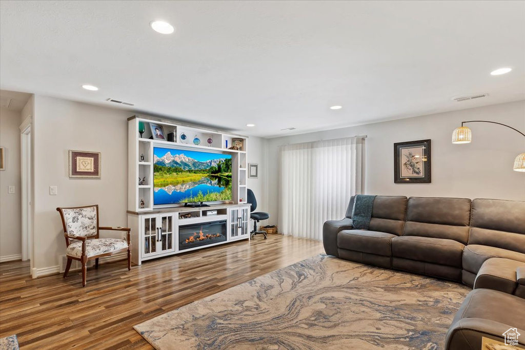 Living room featuring a glass covered fireplace, recessed lighting, visible vents, and wood finished floors