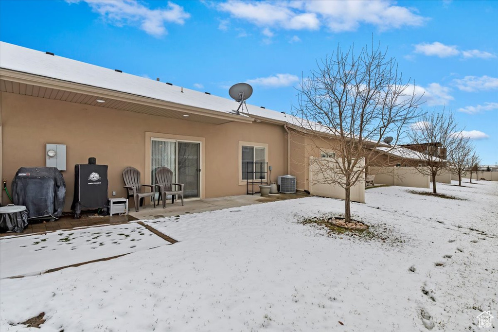 Snow covered rear of property with stucco siding, a patio, and central AC