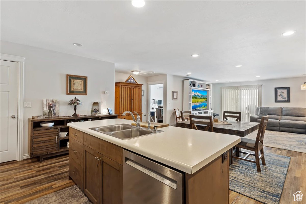 Kitchen featuring a sink, open floor plan, dishwasher, light countertops, and dark wood-style flooring