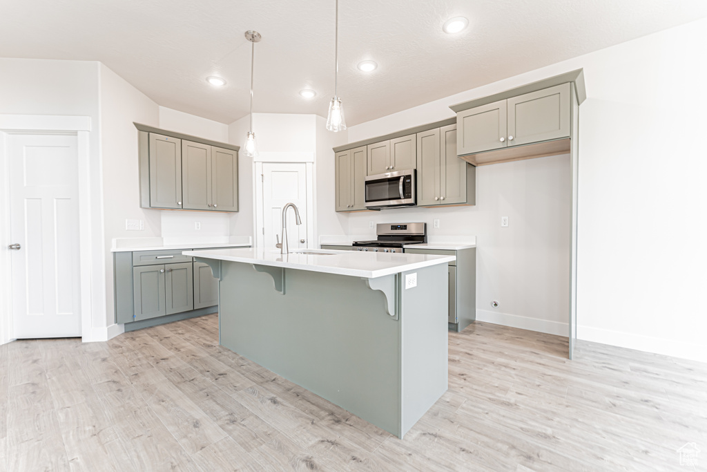 Kitchen with gray cabinets, stainless steel appliances, a breakfast bar, light wood-style floors, and recessed lighting