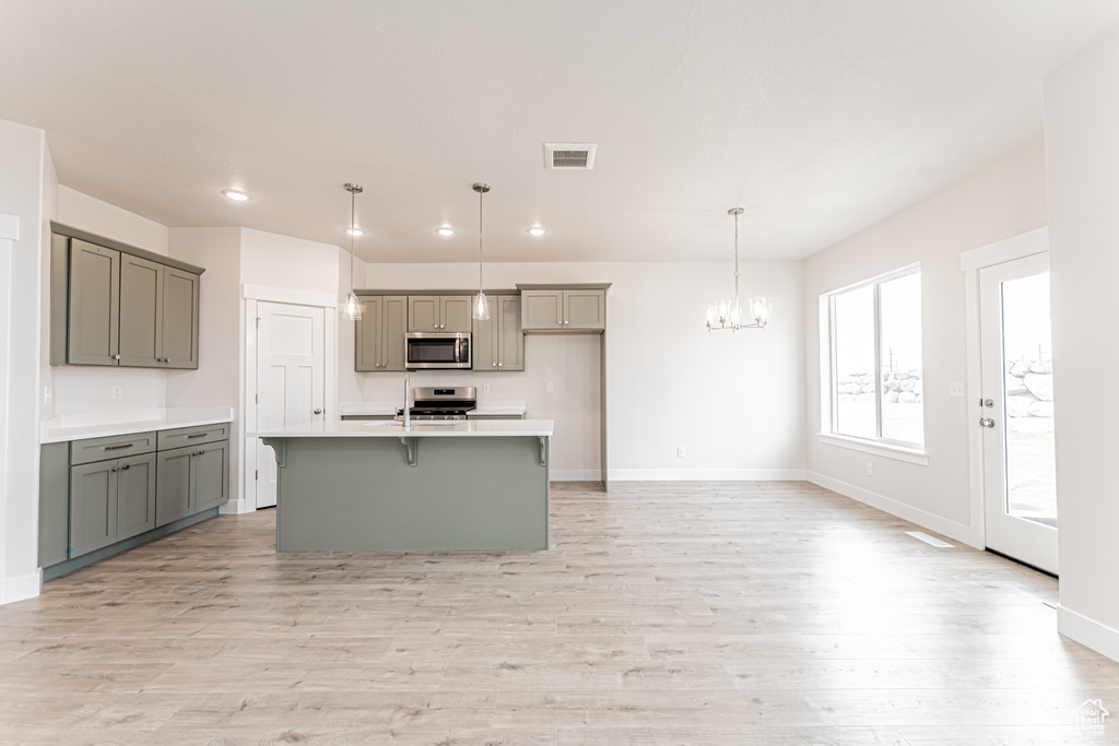 Kitchen with appliances with stainless steel finishes, gray cabinetry, a chandelier, light wood-style floors, and recessed lighting