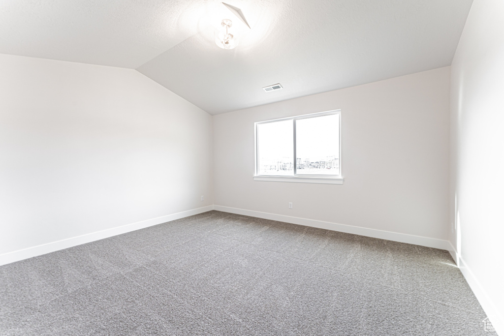 Empty room featuring vaulted ceiling and carpet flooring