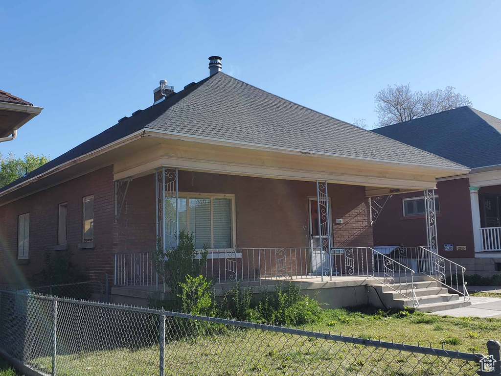 Rear view of house with a porch, brick siding, fence, and roof with shingles