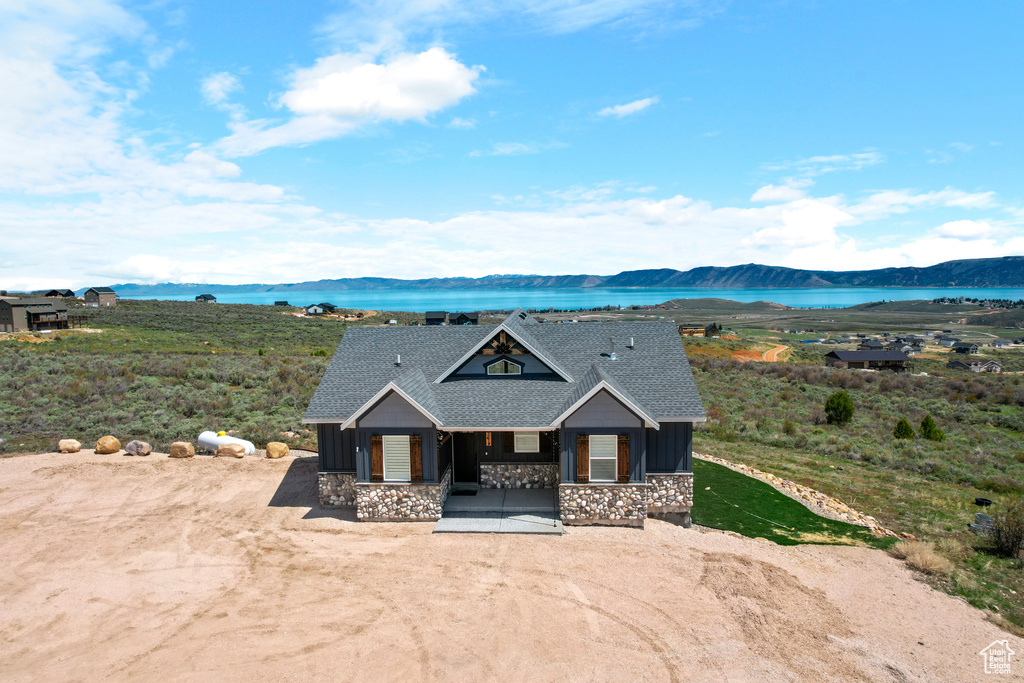 View of front of house featuring stone siding, a water and mountain view, covered porch, board and batten siding, and a shingled roof
