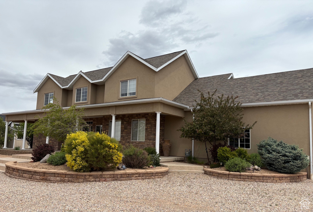 Traditional-style home with stucco siding, roof with shingles, stone siding, and a porch