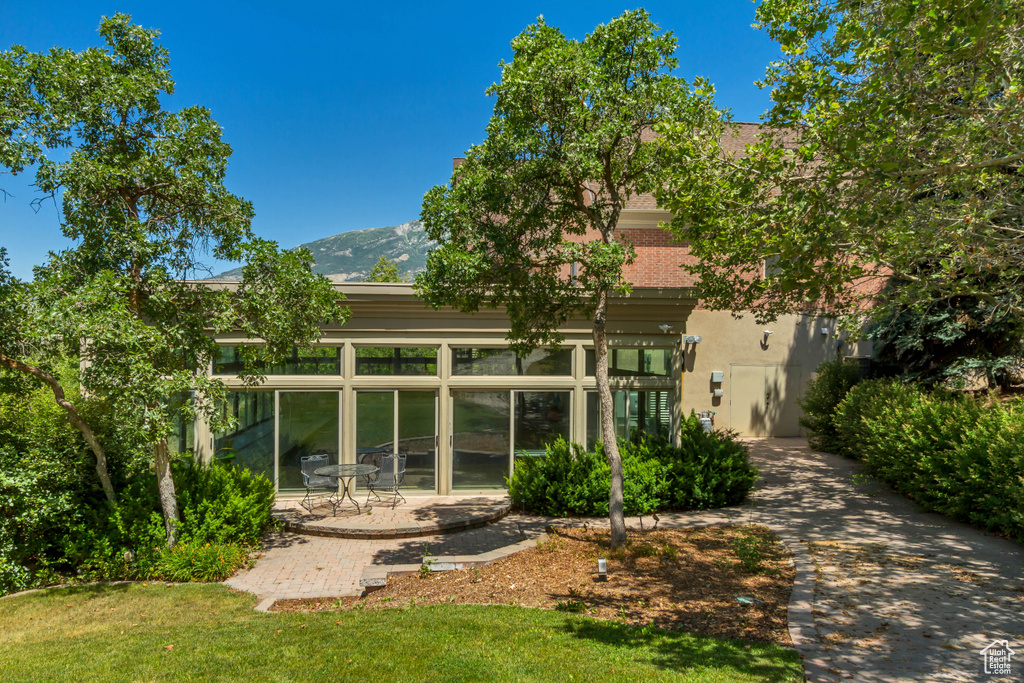 Back of house featuring stucco siding, a mountain view, a yard, a patio, and a sunroom