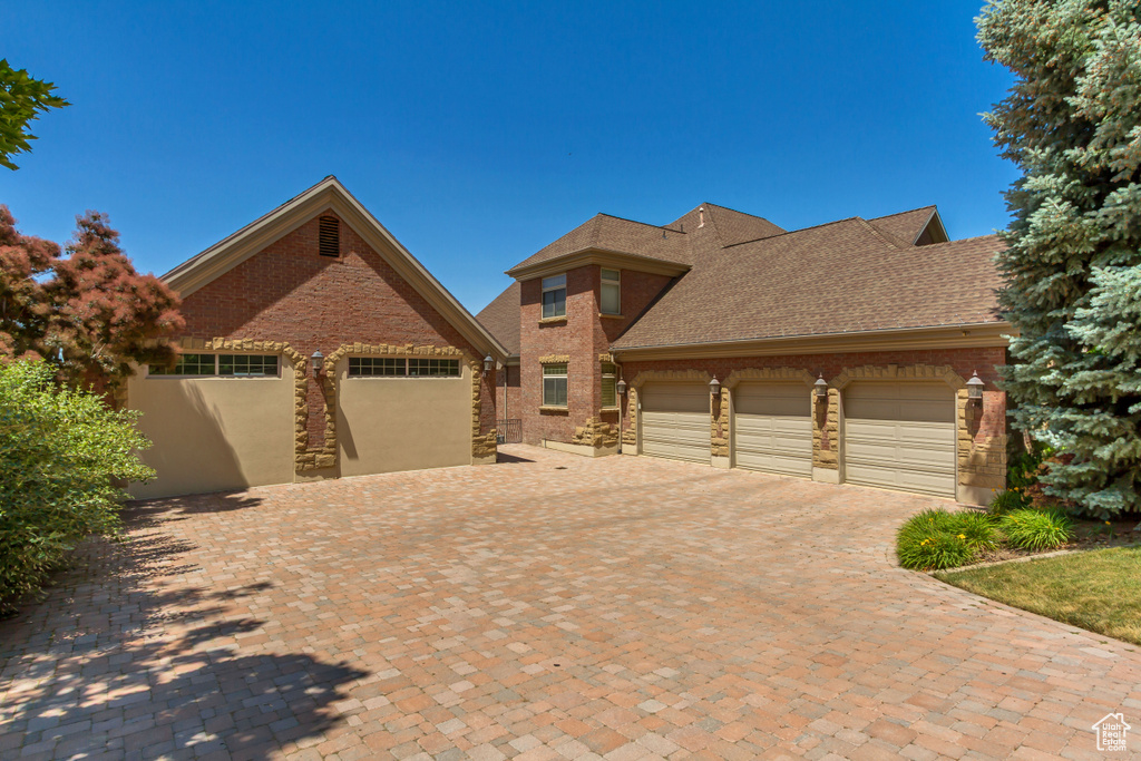 View of front of house with an attached garage, brick siding, driveway, and a shingled roof