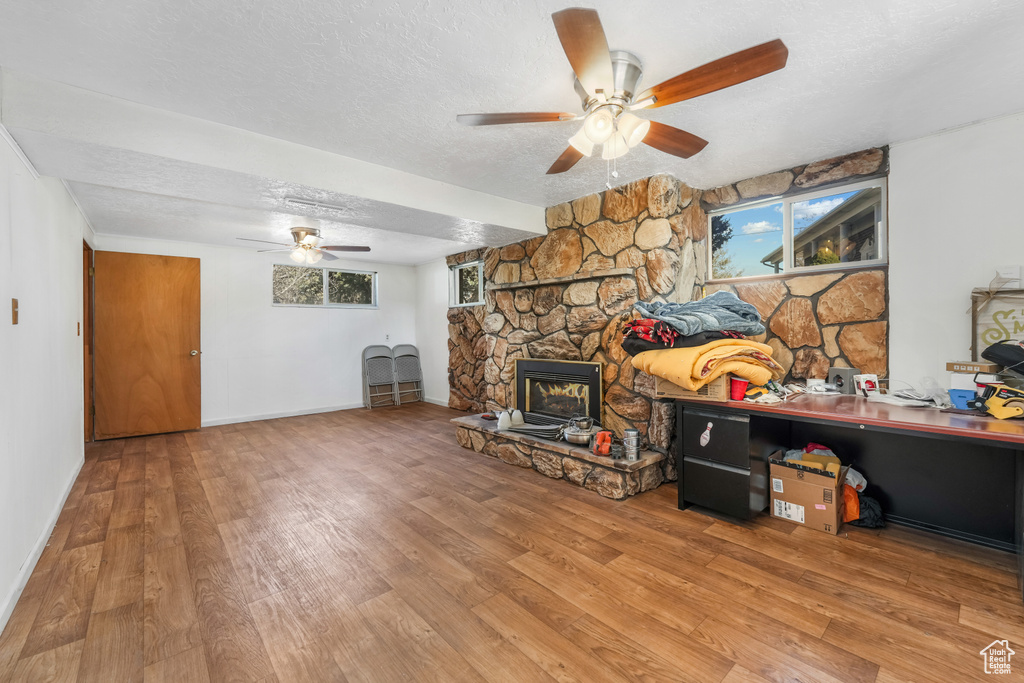 Living area featuring a textured ceiling, a stone fireplace, wood finished floors, and a healthy amount of sunlight