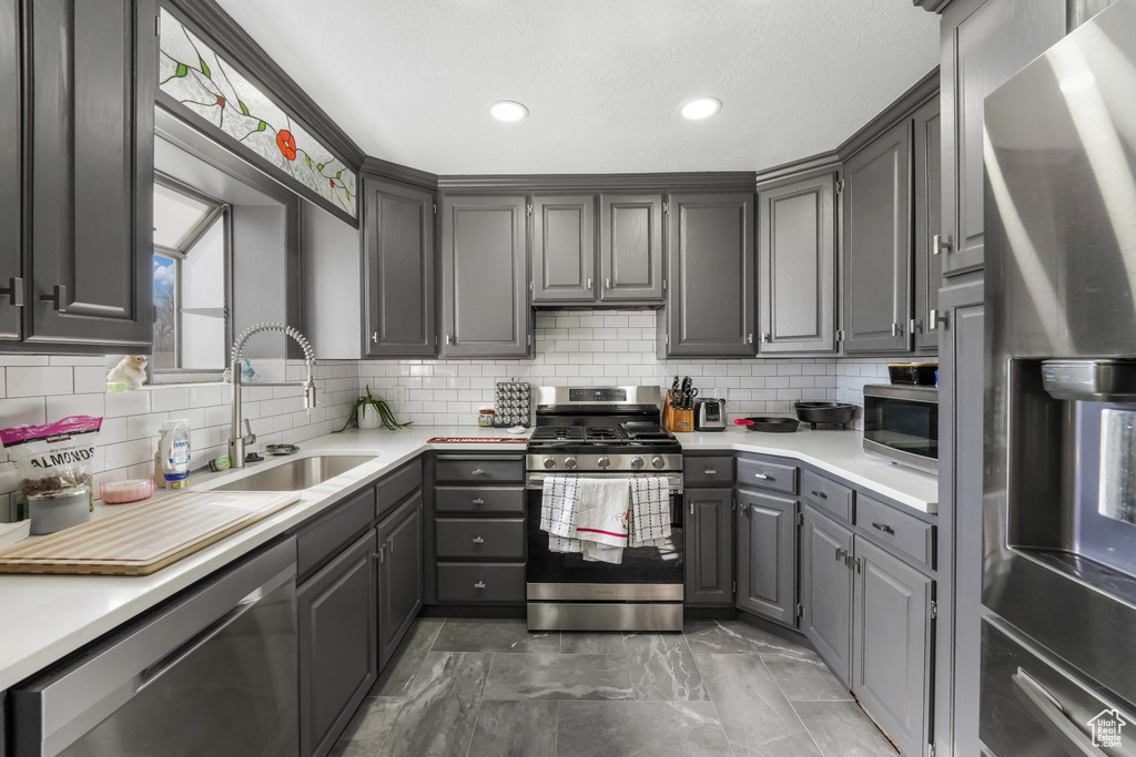 Kitchen with gray cabinets, a sink, stainless steel appliances, light countertops, and decorative backsplash