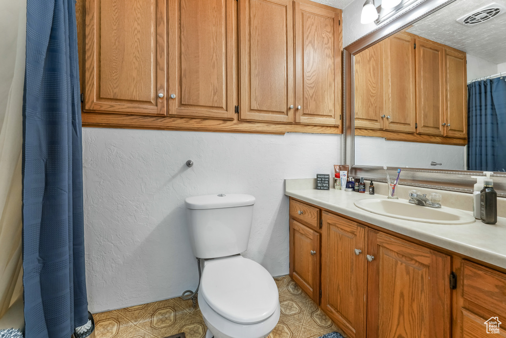 Bathroom featuring visible vents, toilet, vanity, and a textured wall