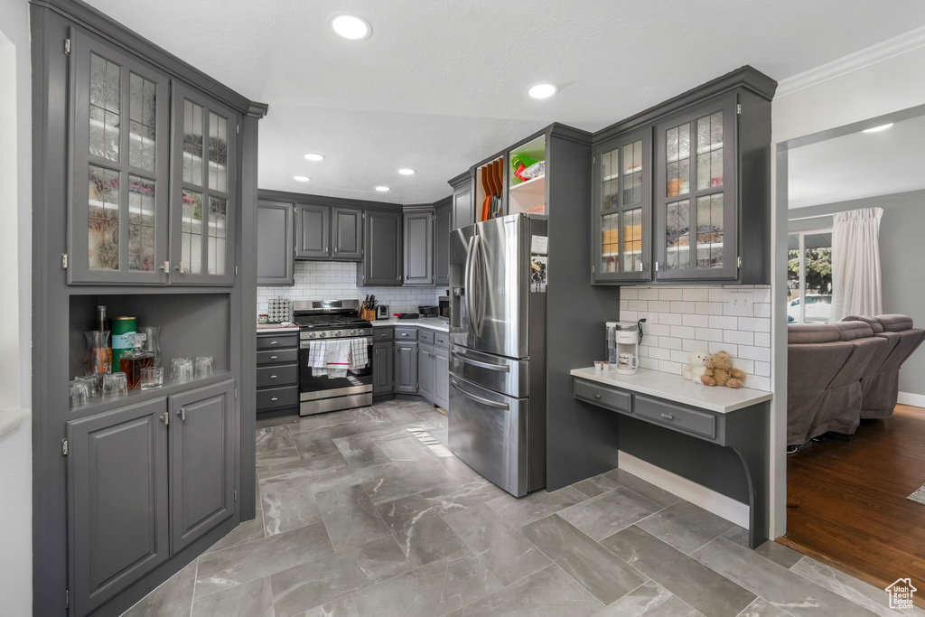 Kitchen with gray cabinetry, light countertops, glass insert cabinets, appliances with stainless steel finishes, and backsplash