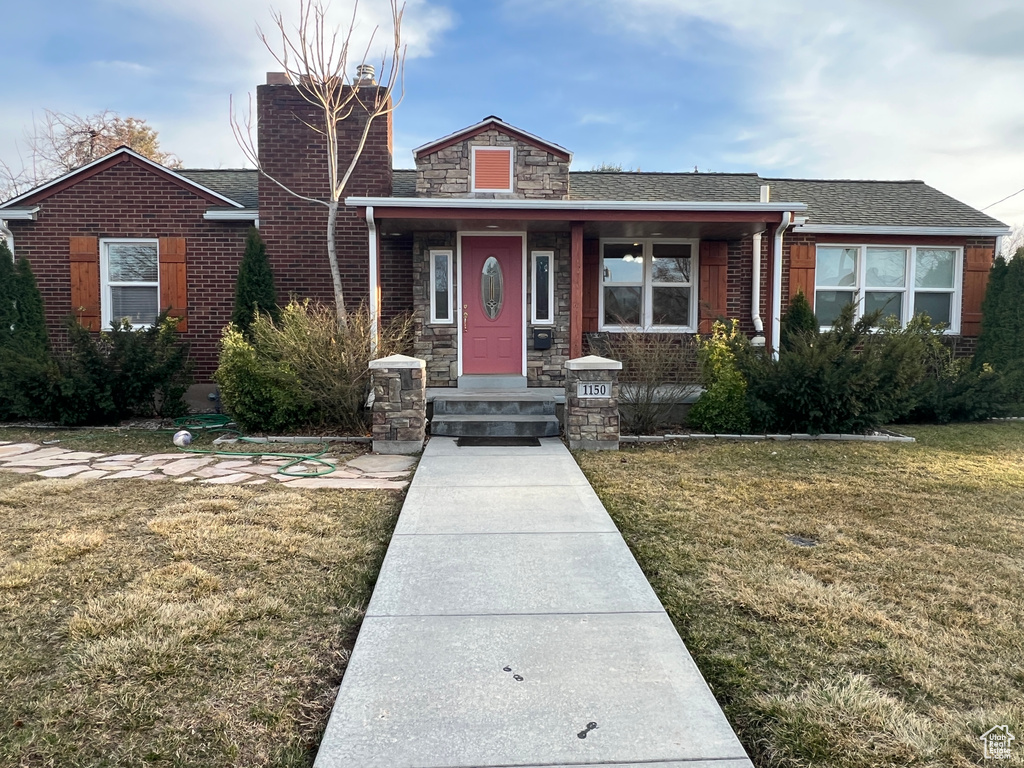 View of front of house featuring a front yard, a chimney, a shingled roof, stone siding, and brick siding