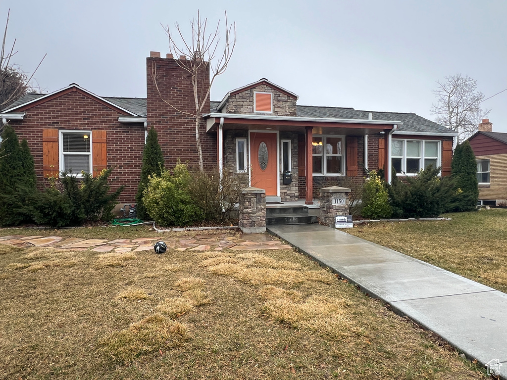 View of front of property with a front yard, brick siding, and a chimney