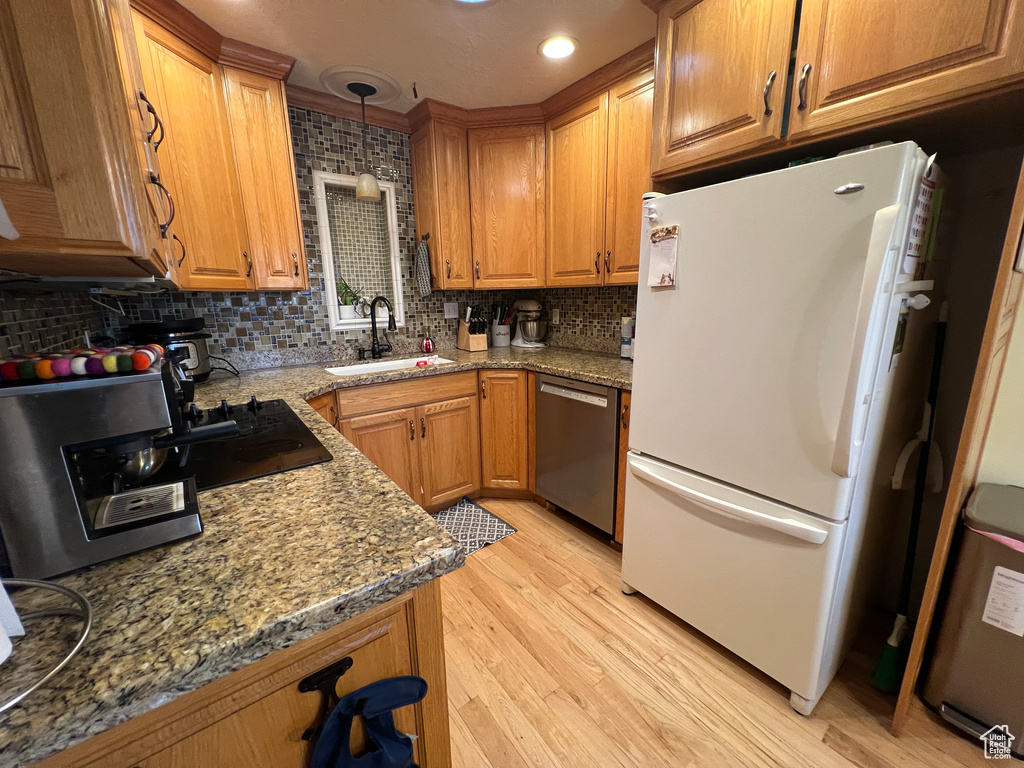 Kitchen with light wood finished floors, brown cabinets, stainless steel dishwasher, freestanding refrigerator, and a sink