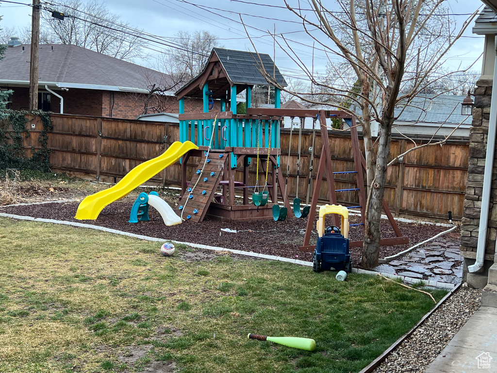 View of jungle gym with a lawn and fence