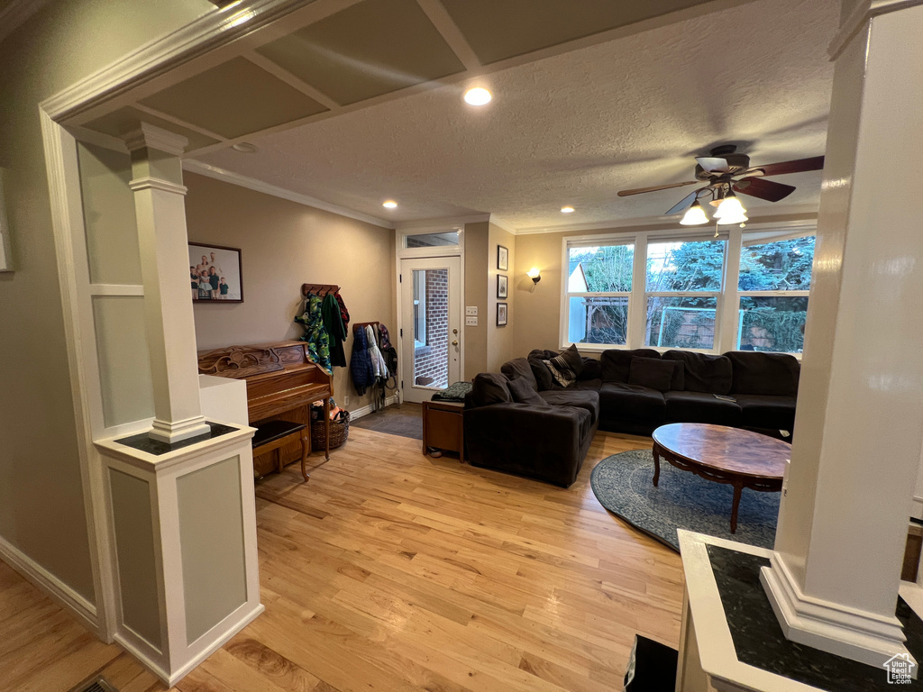 Living area featuring light wood-style flooring, ornamental molding, and ornate columns