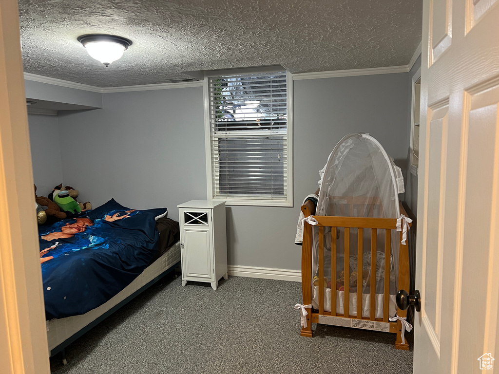 Bedroom featuring baseboards, a textured ceiling, ornamental molding, and carpet