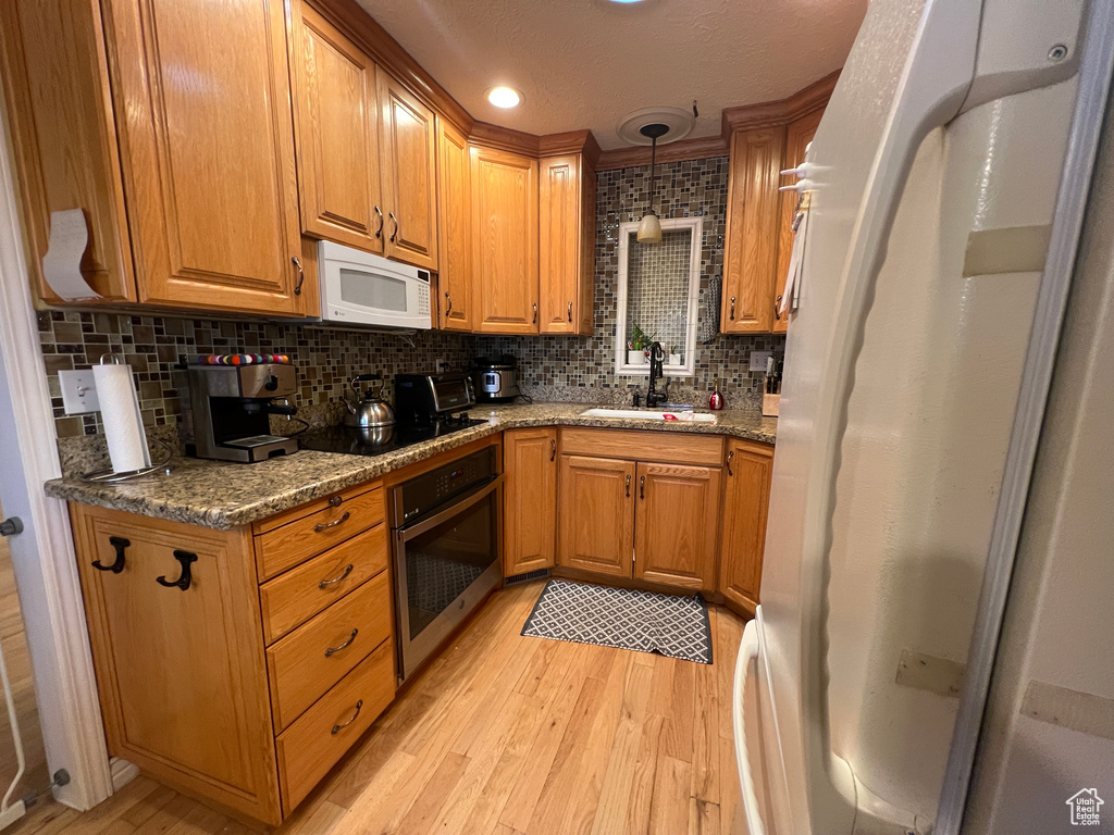 Kitchen featuring a sink, decorative backsplash, white appliances, and light wood-style floors