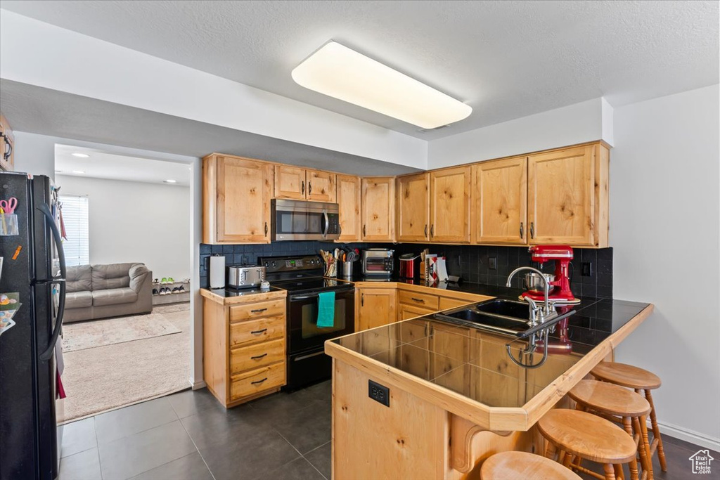 Kitchen with black appliances, a kitchen breakfast bar, a peninsula, decorative backsplash, and dark tile patterned floors