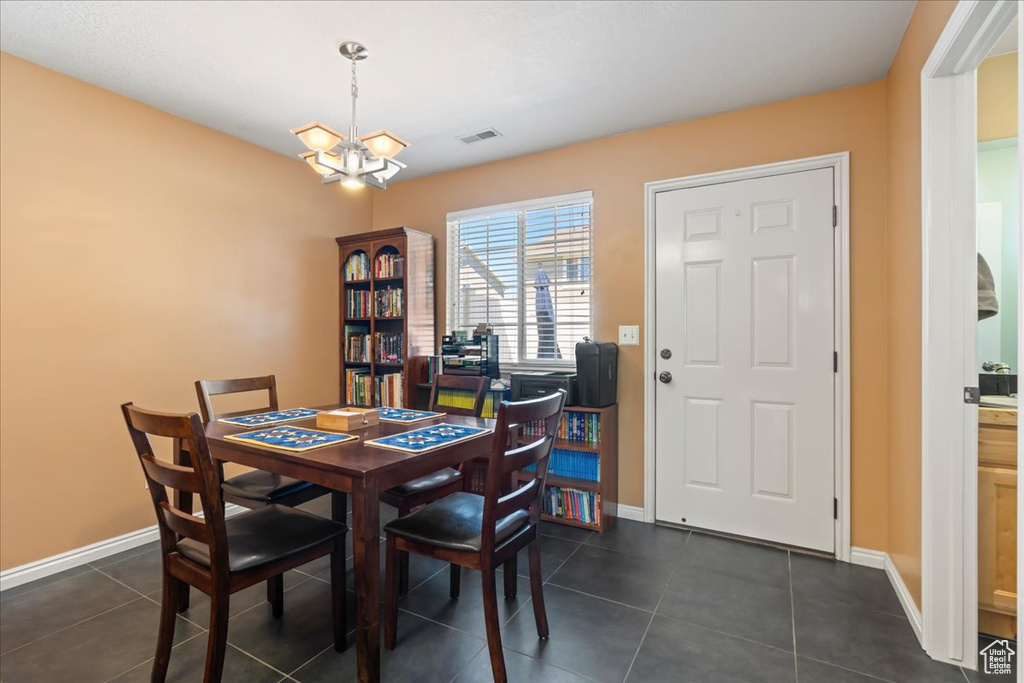 Dining room with a chandelier, dark tile patterned flooring, visible vents, and baseboards