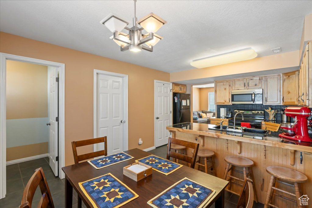 Dining room with a textured ceiling, dark tile patterned floors, baseboards, and an inviting chandelier