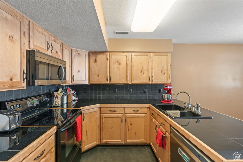 Kitchen featuring appliances with stainless steel finishes, light brown cabinets, a sink, and tile countertops