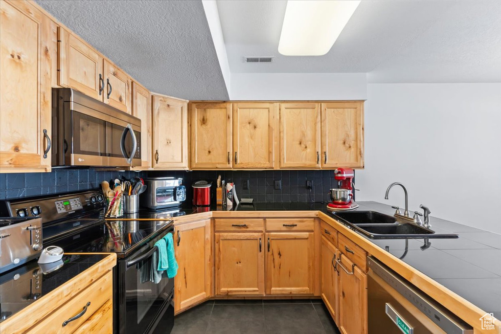 Kitchen with appliances with stainless steel finishes, tile counters, light brown cabinetry, decorative backsplash, and dark tile patterned floors