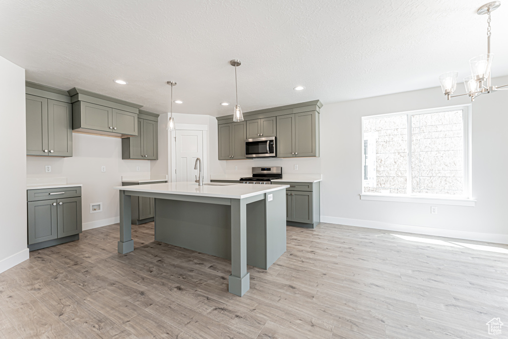 Kitchen with stainless steel appliances, gray cabinets, light wood-style flooring, a chandelier, and light countertops