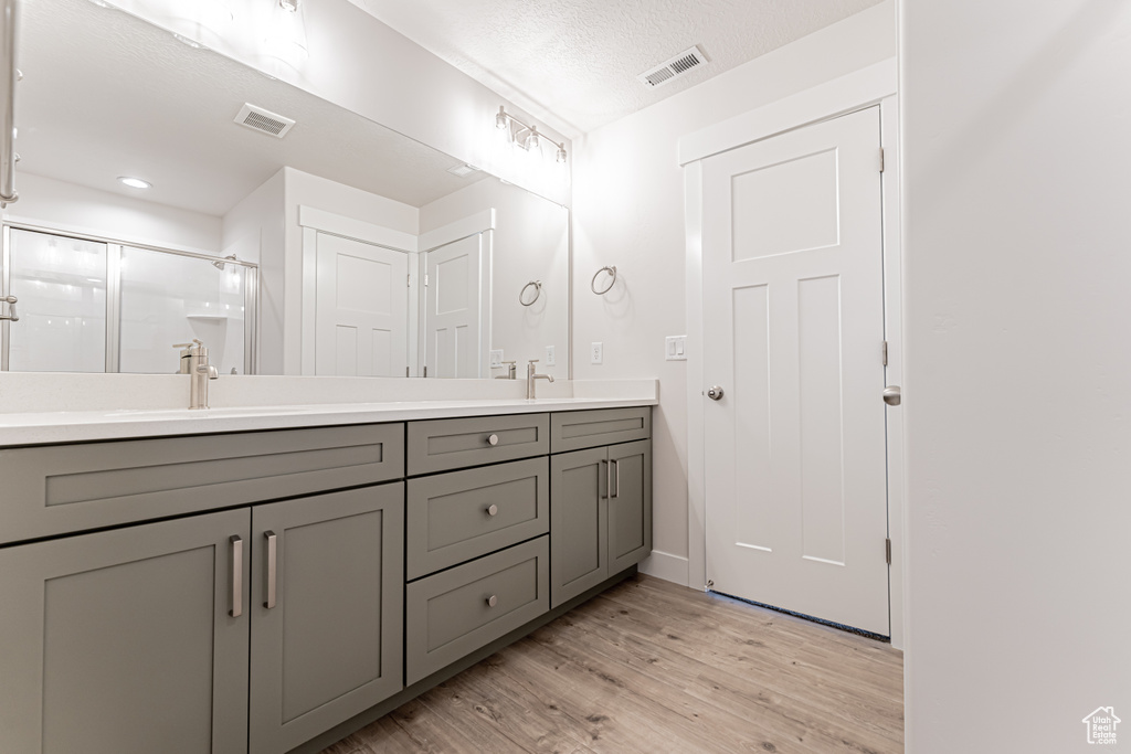Bathroom featuring double vanity, wood finished floors, a shower stall, and a textured ceiling