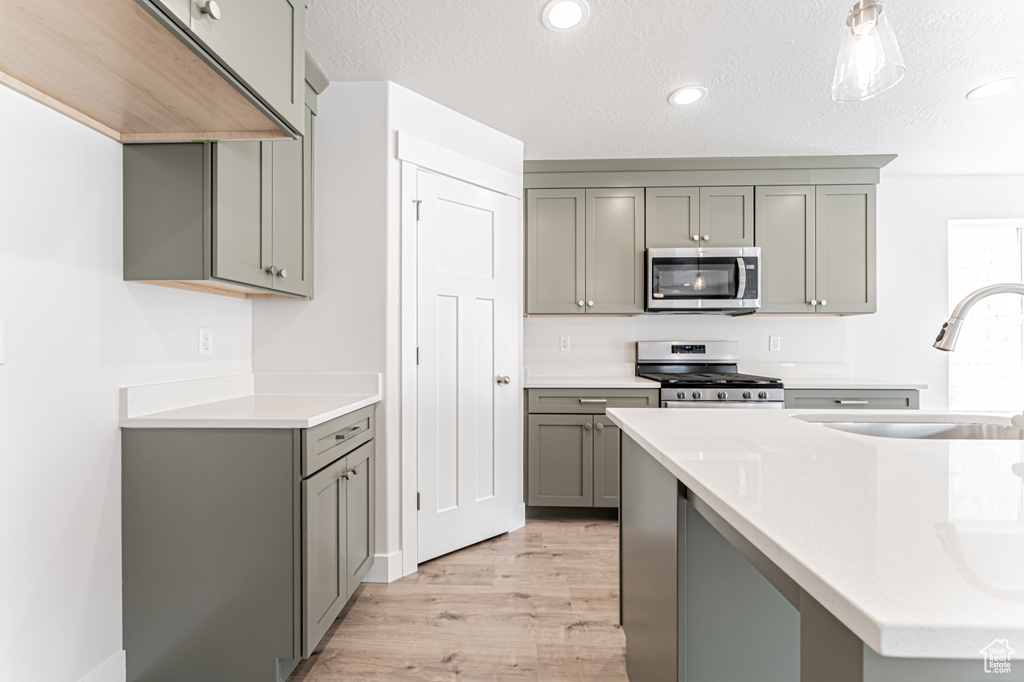 Kitchen featuring stainless steel appliances, gray cabinets, light wood-style flooring, light countertops, and a textured ceiling