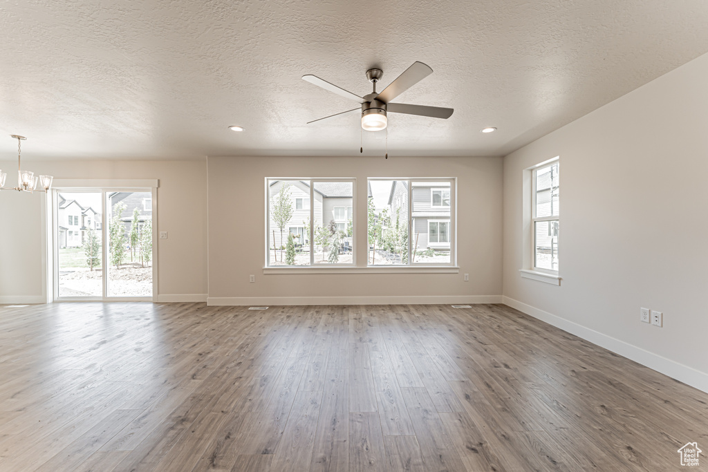 Spare room featuring a textured ceiling, healthy amount of natural light, wood finished floors, a chandelier, and a ceiling fan