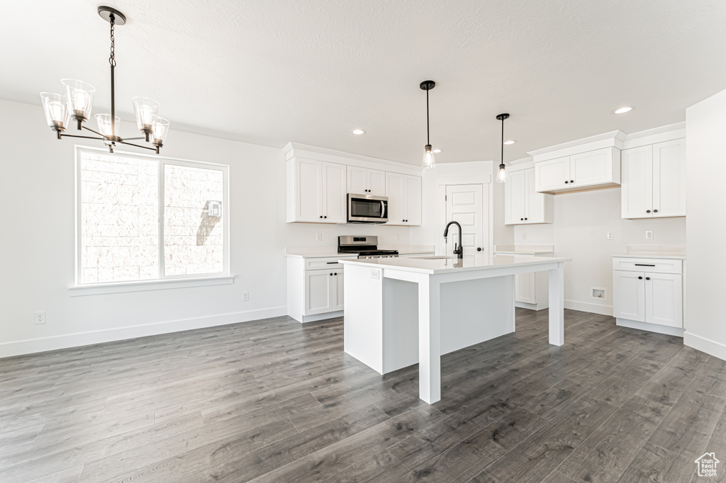 Kitchen featuring stainless steel appliances, a chandelier, wood finished floors, white cabinetry, and light countertops