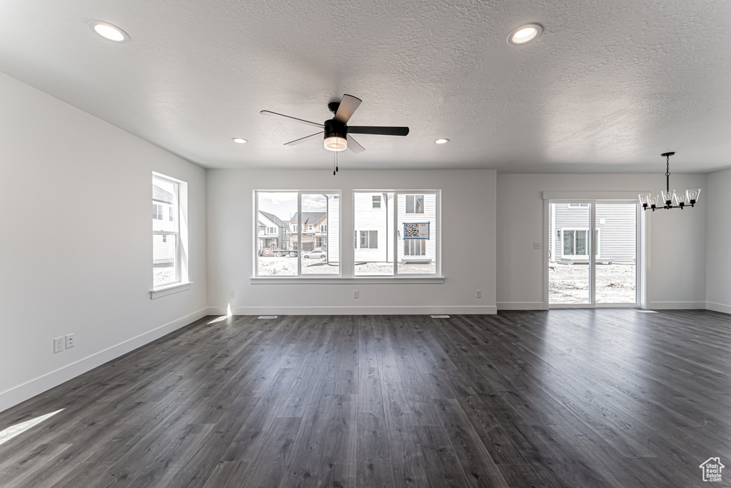 Unfurnished living room with a chandelier, ceiling fan, plenty of natural light, dark wood-style floors, and a textured ceiling