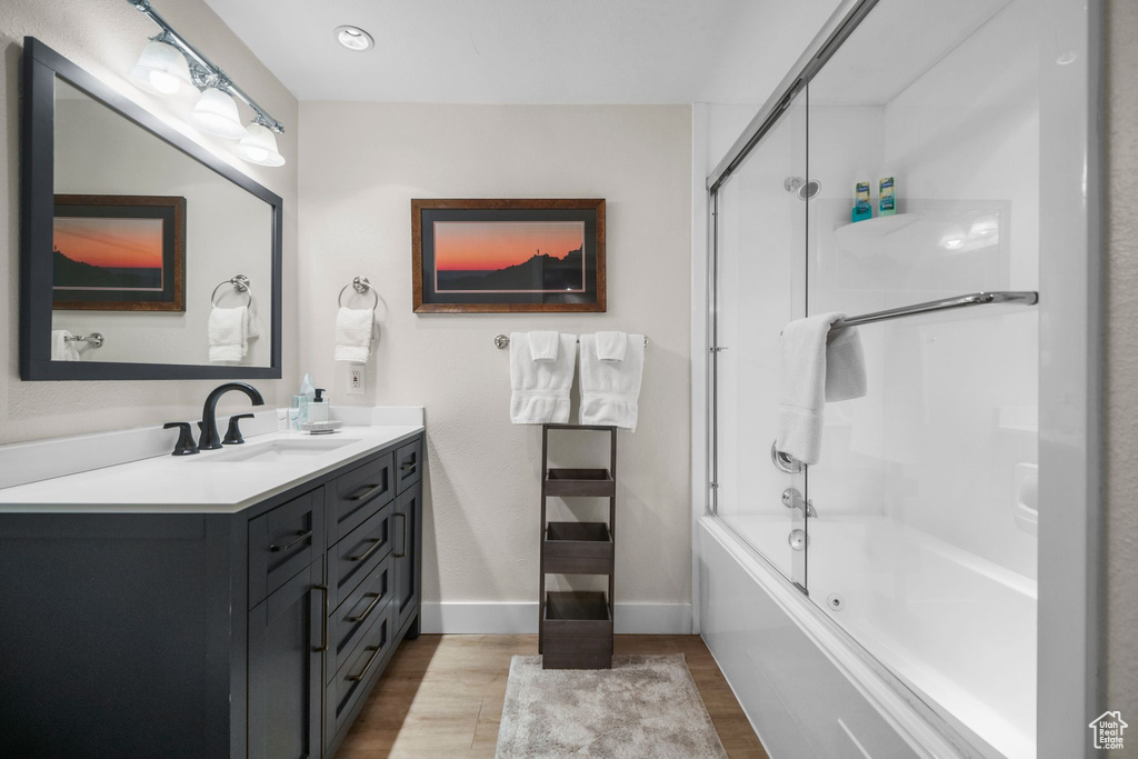 Bathroom featuring combined bath / shower with glass door, baseboards, wood finished floors, and vanity