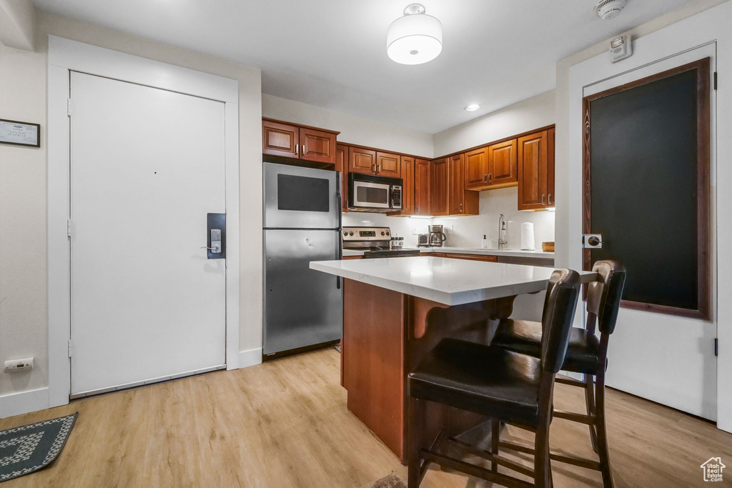 Kitchen with stainless steel appliances, a kitchen bar, a kitchen island, and light wood finished floors