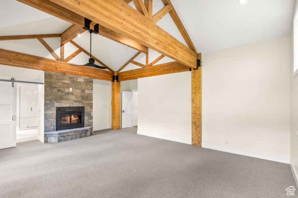 Unfurnished living room featuring beamed ceiling, high vaulted ceiling, a barn door, a fireplace, and carpet flooring